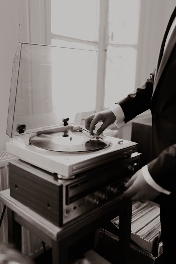 A man in a suit using a vintage record player indoors. Classic black and white setup.